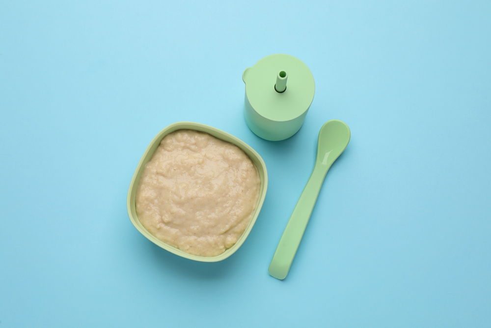 Healthy baby food in bowl and bottle with drink on light blue background, flat lay