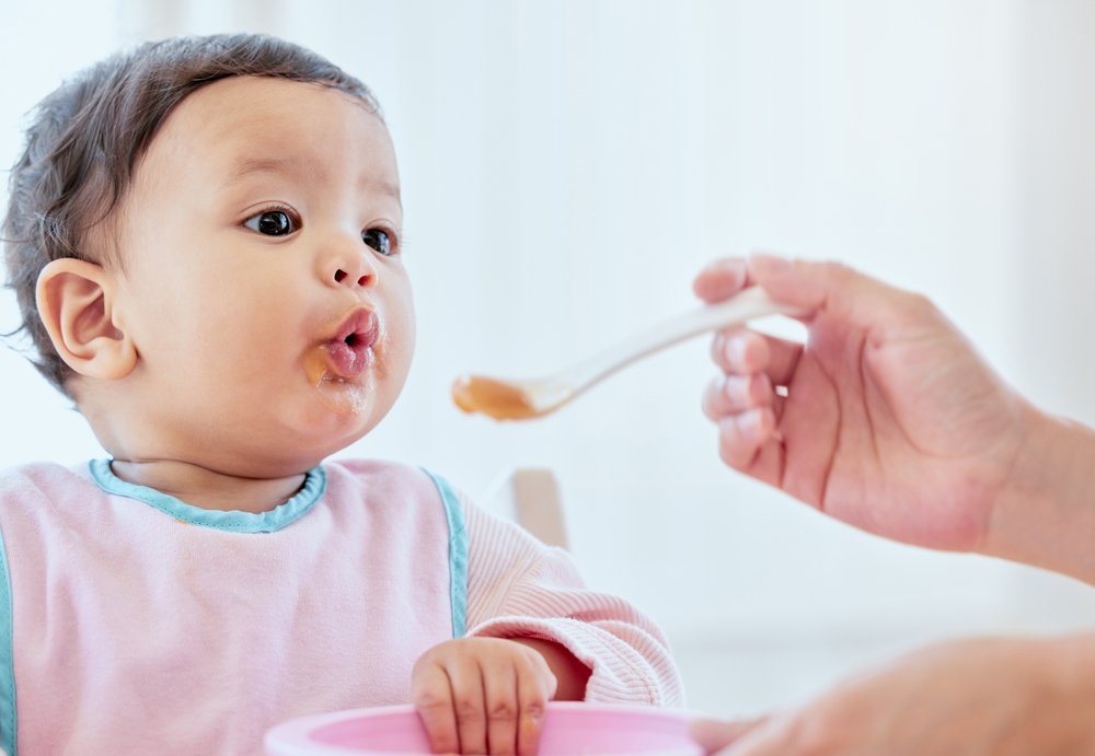 The cutest pout. Shot of an unrecognizable woman feeding her baby girl at home.