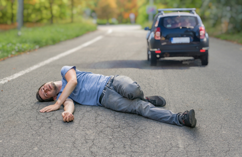 man lying injured on a road while a car drives away