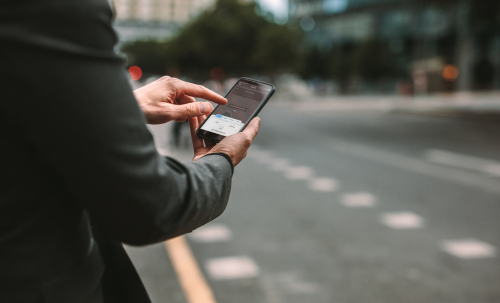 Commuter using a rideshare app on a phone near the street, illustrating a Rideshare Crash in NYC scenario.