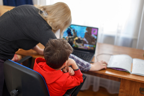 Child gaming on a laptop while an adult supervises, illustrating concerns related to a Roblox Addiction Lawsuit.