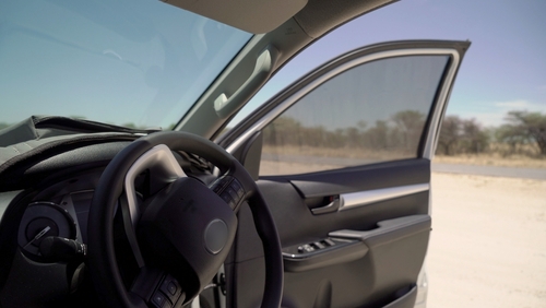 car parked on the roadside with the driver&rsquo;s door open and bright sunlight casting shadows inside the vehicle