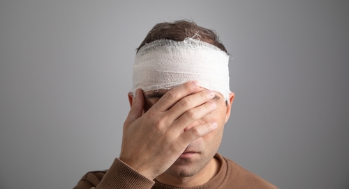 injured man with a bandaged head holding his forehead in pain
