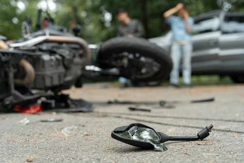 man lying beside a fallen motorcycle on the road with broken mirror glass in the foreground