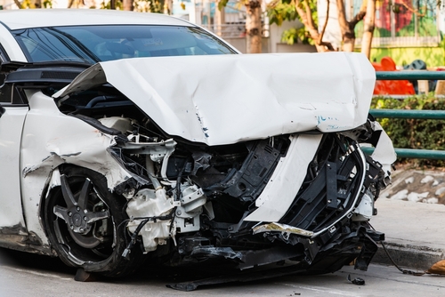 front end of a white car crushed after a severe crash on a city street