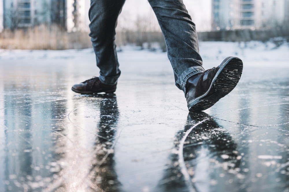 Boots standing on icy ground, illustrating the danger of slipping on a frozen, slippery winter surface. A man walks cautiously along an icy street on a winter day for fear of slipping and falling.