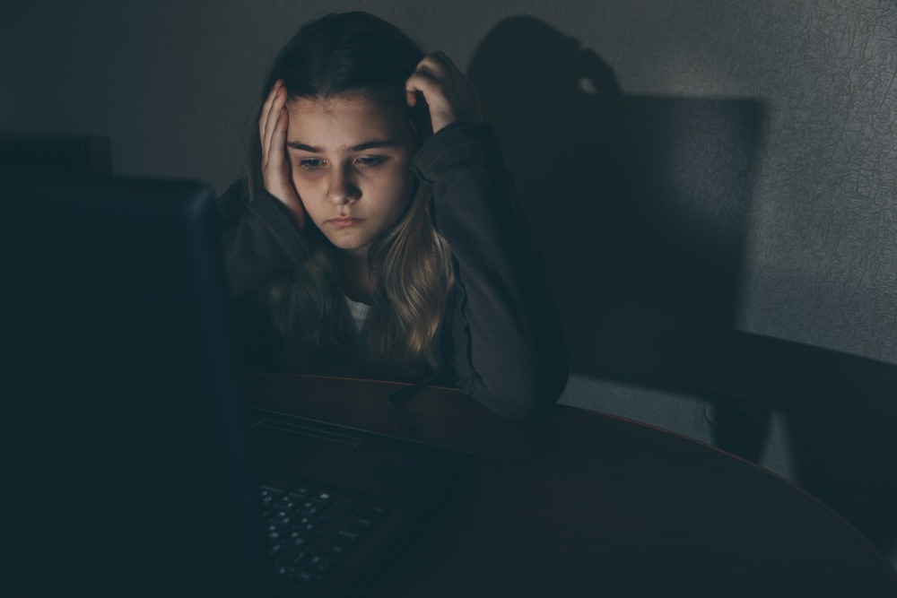 Teen girl looking distressed while using laptop at night, representing online grooming risks on platforms like Discord